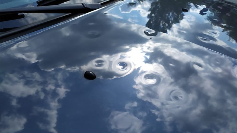 Motorhaube eines grauen PKW mit Hagelschaden